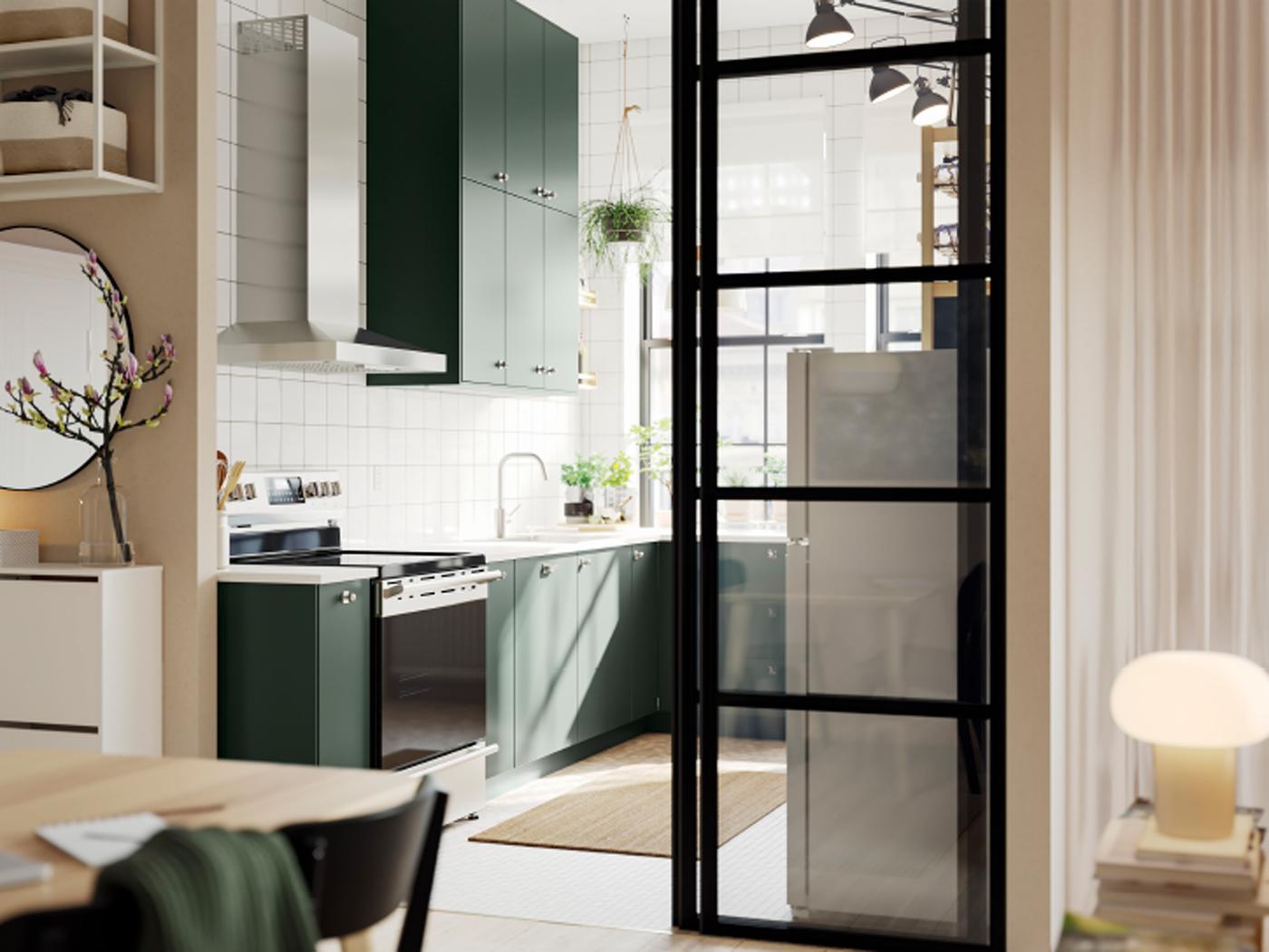 An open kitchen with deep green HAVSTORP kitchen fronts and wall cabinets up to the ceiling, next to a bright living room.