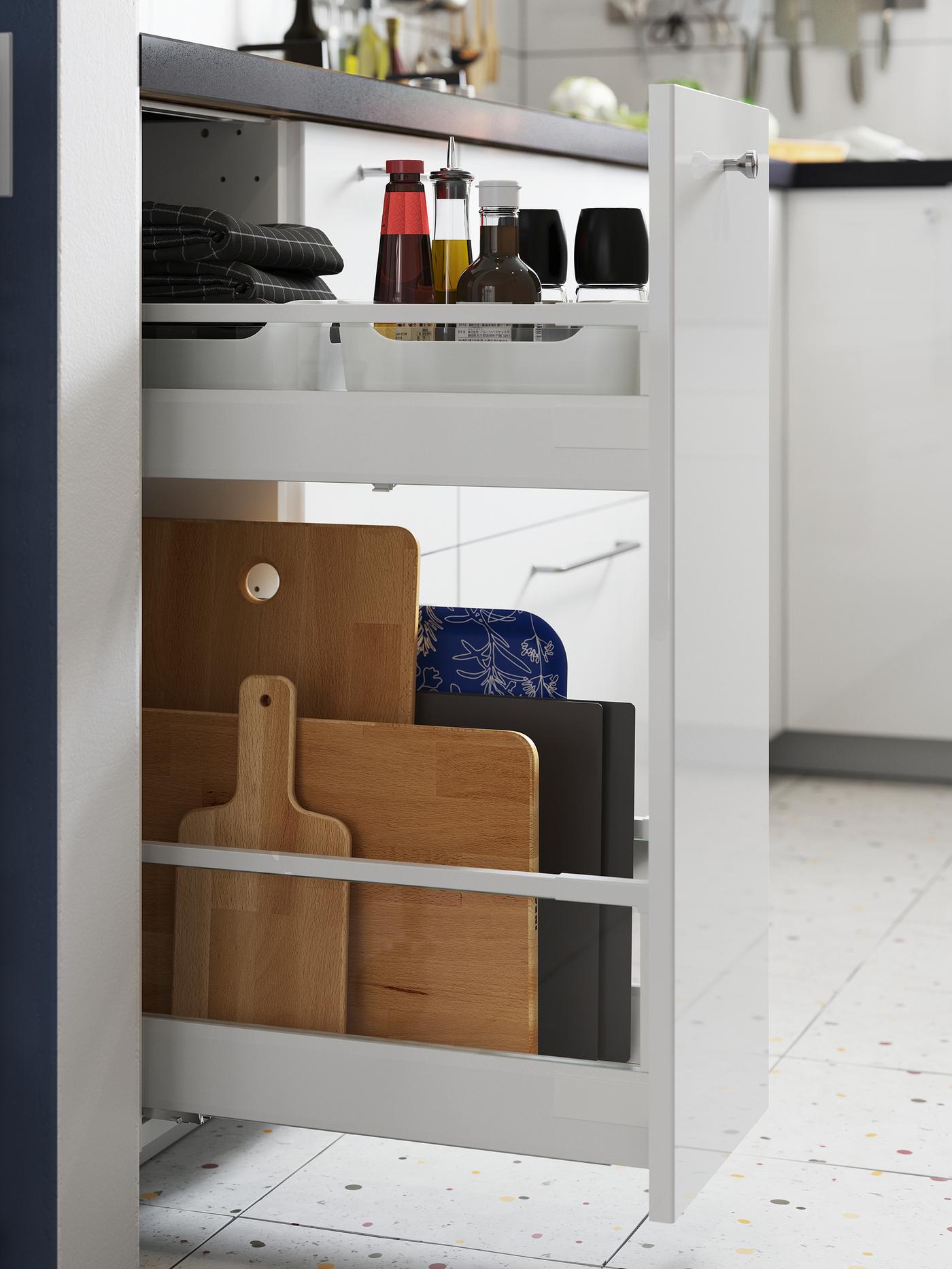 An open narrow pull-out cabinet with chopping boards on the lower shelf and oils and condiments on the upper one.