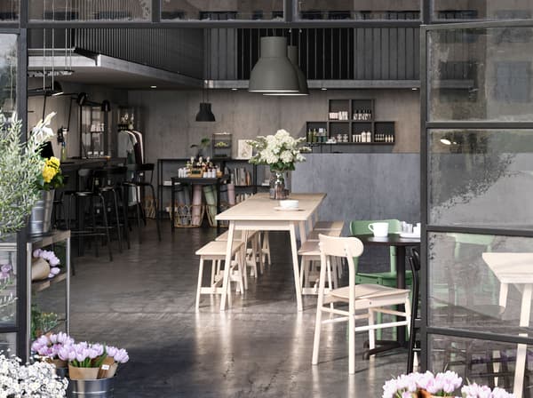 An open plan cafe, shop and co-working space framed by open glass doors. Flowers are on the table and by the doors.