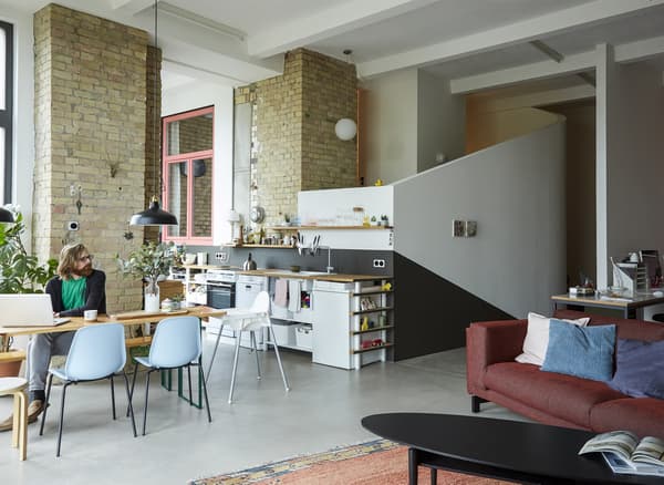 An open-plan living room, kitchen, and dining space in a converted loft with brick walls.
