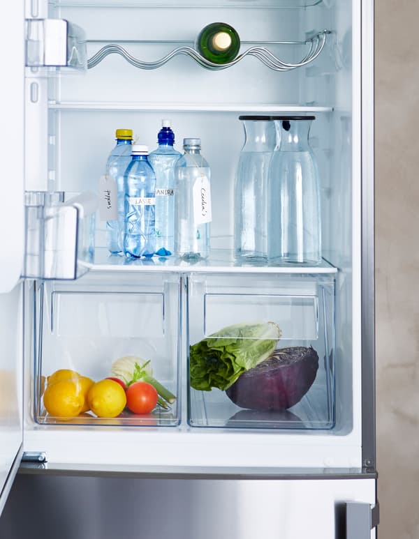 An open refrigerator door reveals individual bottles of water and several carafes filled with water.