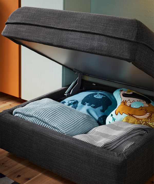 An open VALLENTUNA storage seat section with Hillared dark grey cover holds blankets and pillows.