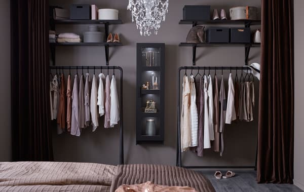 An open wardrobe consisting of black hanging racks, black open shelves and a black display cabinet, filled with clothes.