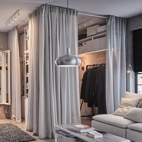 An open wardrobe solution, light grey GUNRID curtains, a black clothes rack and a white sofa with grey cushions.
