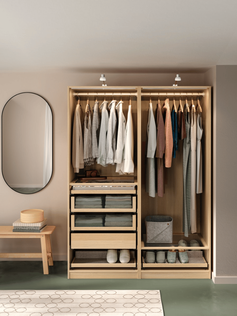An open wooden wardrobe with clothes hangers in a bedroom with a mirror on the wall.