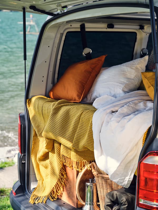 An orange and off-white cushion laying on top of multiple blankets in the back of a van