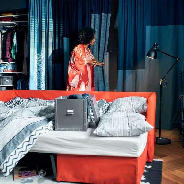 An orange sofa transformed into a sofa bed, with grey bedlinen and a woman in the background.