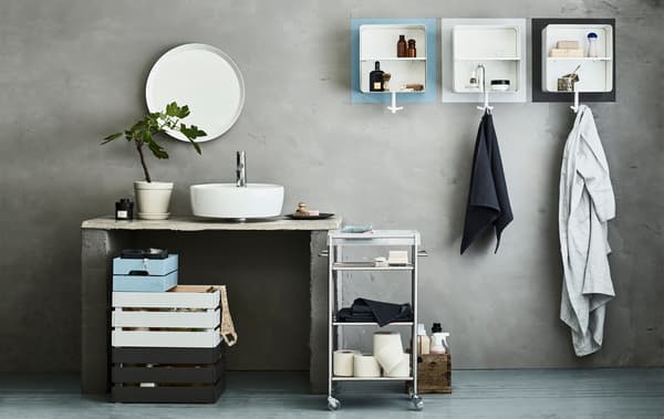 An organised shared bathroom with different coloured KNAGGLIG wooden boxes, a GRUNDTAL trolley and wall cabinets.