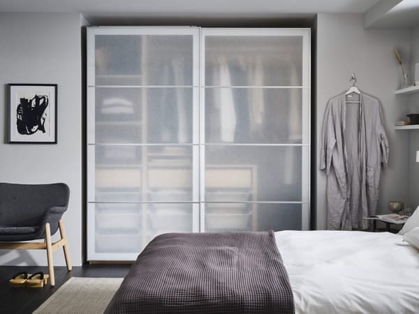 An organized bedroom with a wardrobe behind sliding doors and a robe to the side of it.