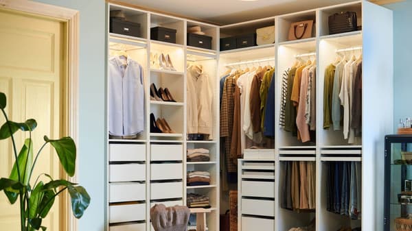 An organized, white wardrobe with clothing and accessories in a corner of a room.
