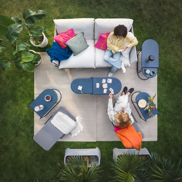 An oudoor lounge area in the garden, with white sofas and bright orange pillows, featuring GRYTSHOLM nest of tables.