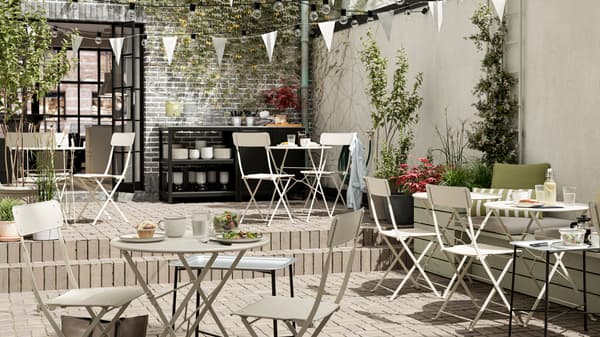 An outdoor cafe with beige steel foldable tables and chairs, white bunting, tiled floors and a serving station.