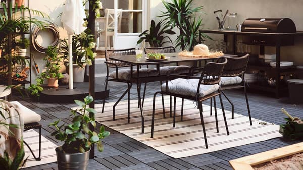 An outdoor dining table with dark gray RUNNEN outdoor decking under the table and chairs.