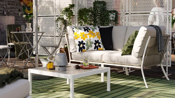 An outdoor lounge area with a SEGERÖN sofa and coffee table. There are green outdoor rugs and privacy screens with plants.