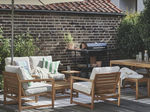 An outdoor seating area with modern wooden furniture, white cushions, and green striped pillows and a wooden table next to it.