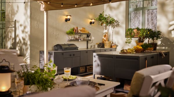 An outdoor space with a white/beige BONDHOLMEN table and several BÅTSKÄR units in dark grey including a charcoal barbecue.