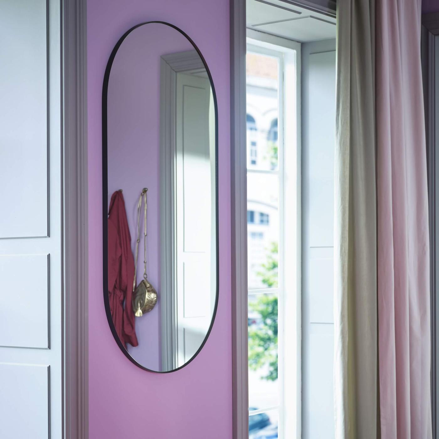 An oval shaped mirror in a room with a pink wall.