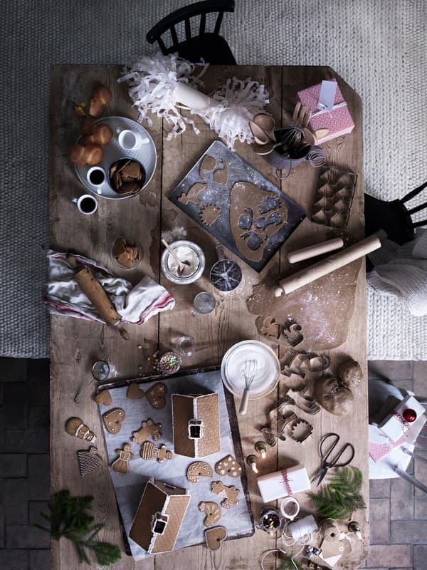 An overhead view of a large wood harvest table, filled with baking supplies, ingredients and tools to make gingerbread cookies.