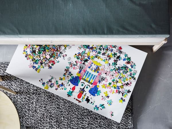 An overhead view of a puzzle on a board that’s sticking out from under a sofa.