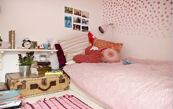 An overview of a teen's bedroom with white and pink patterned bedlinens and a vintage suitcase used as a bedside table.