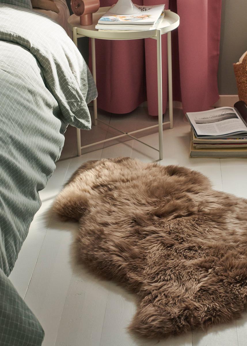 An ULLERSLEV sheep skin lying next to a bed. 