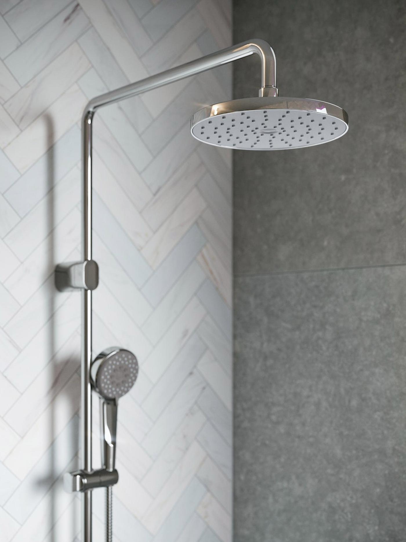 An unhappy spaniel puppy being rinsed with a hand shower while sitting on the black and white tiled floor of a bathroom.