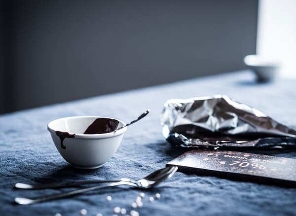 An unwrapped chocolate bar, melted chocolate in a bowl and a spoon for creating spoon shaped homemade chocolate gifts.