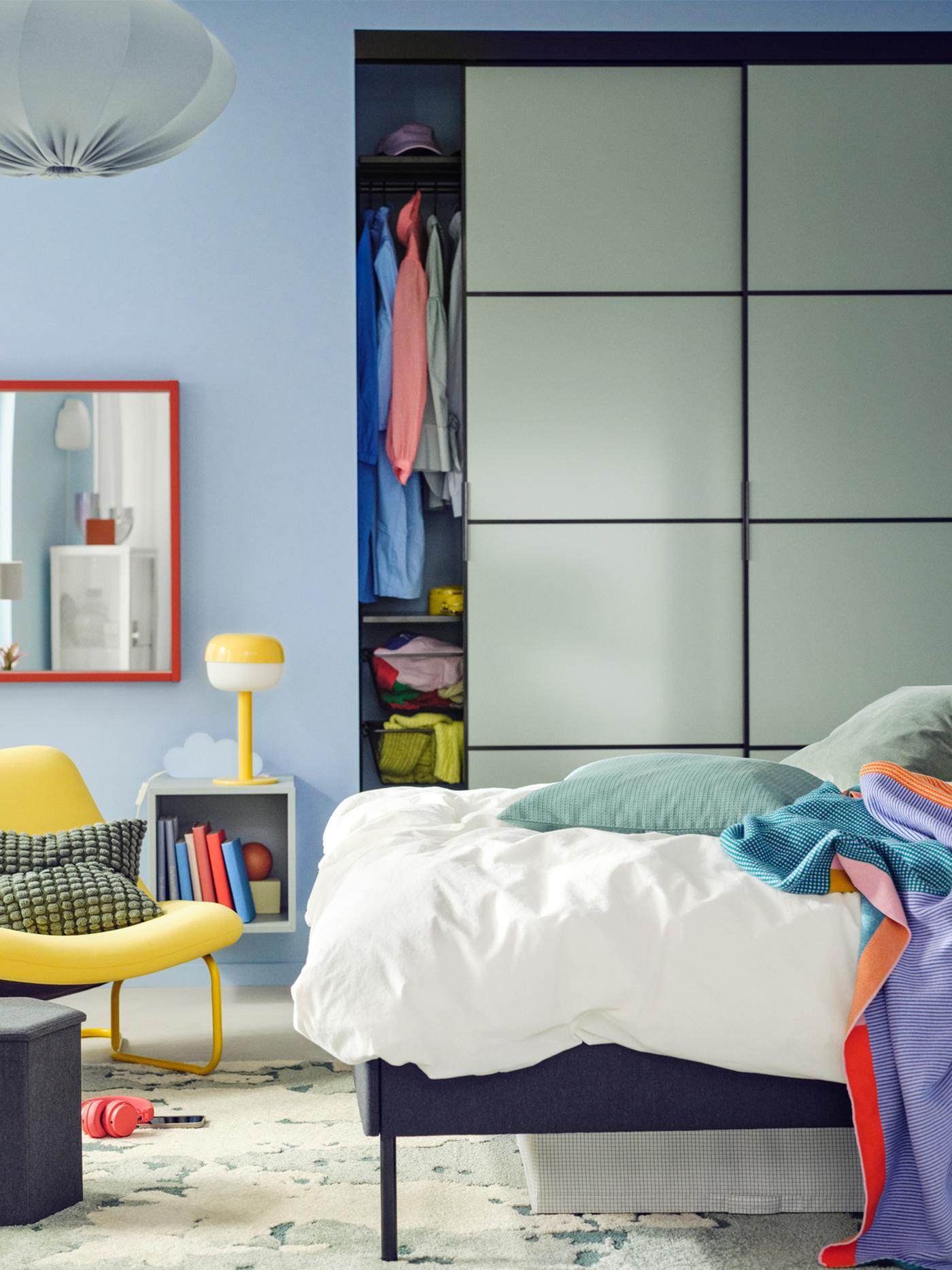 An upholstered bed with ÄNGSLILJA bed linen stands in front of a SKYTTA/BOAXEL reach-in wardrobe with sliding doors.