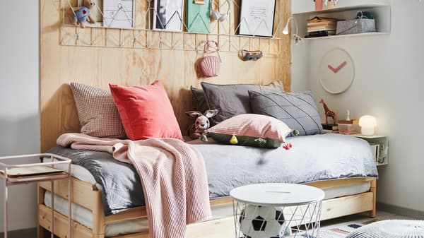 An UTÅKER stackable bed with lots of cushions and textiles on, surrounded by a bedside table, storage and decorations.