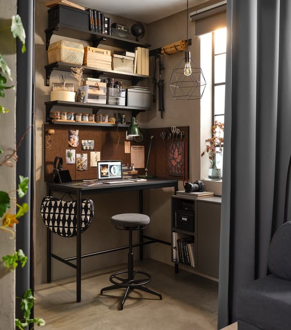 Angolo di una stanza ben organizzato con varie mensole piene di materiali artistici, un tavolo e uno sgabello, dietro una tenda usata come divisorio. 