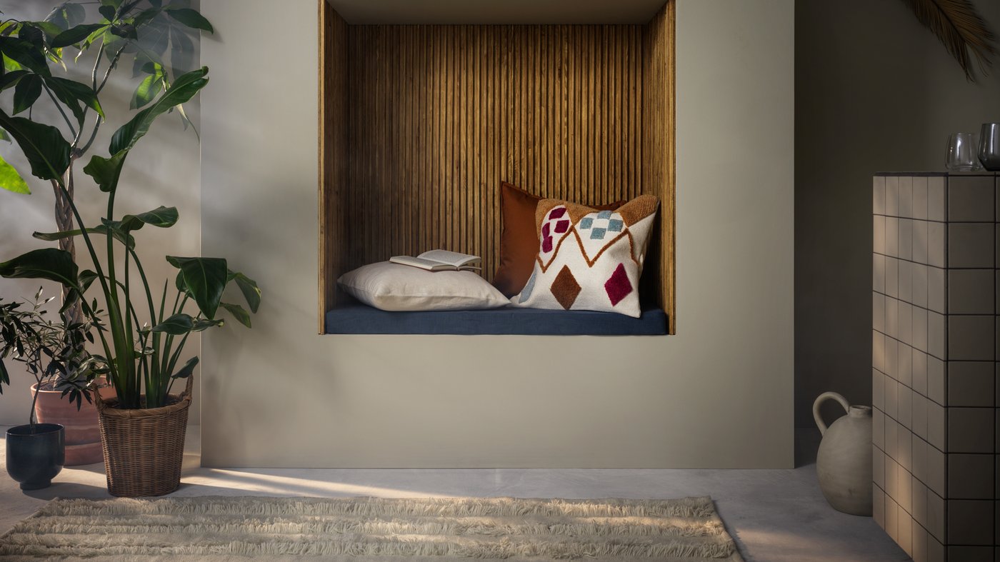 Angolo lettura incassato nella parete con cuscini; ai lati, vasi di piante frondose da una parte e un vaso dall'altra.