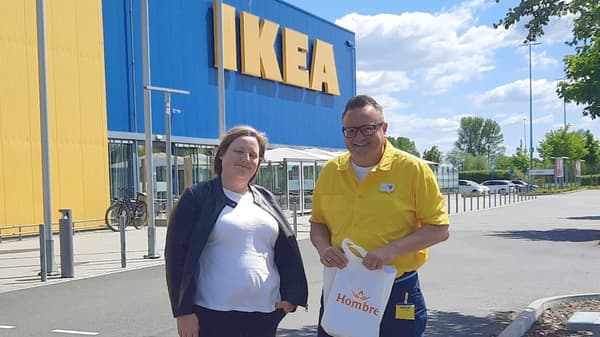Anika Langer von HOMBRE und Alexander Seidlich von IKEA stehen vor dem IKEA Einrichtungshaus in Bremerhaven. Alexander Seidlich hält symbolisch einen Beutel mit Aufdruck des HOMBRE Logos.