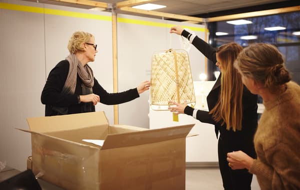 Anna Granath holds up a woven lamp above a large box while two other people look at it.