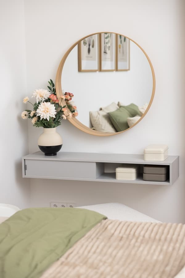 Apaļš spogulis virs sienas galdiņa ar dekoratīviem priekšmetiem guļamistabā.