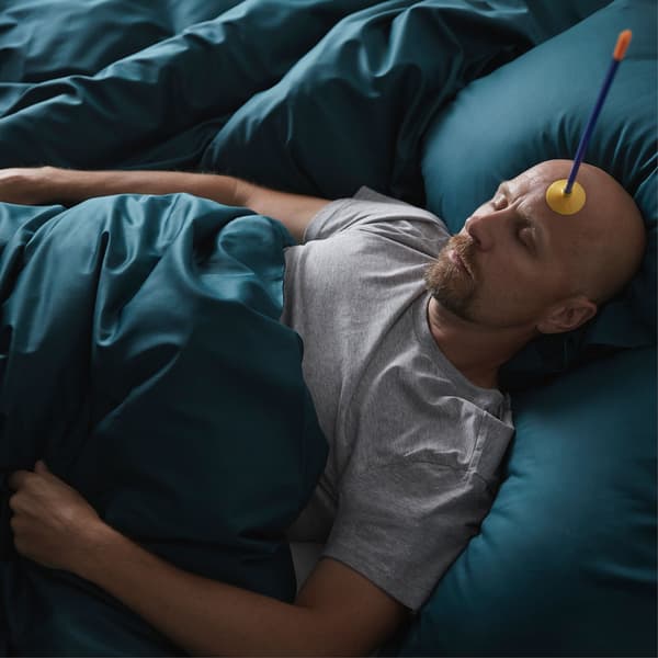 Aparece un home durmido nunha cama de aspecto acolchado cunha frecha de xoguete con ventosa na fronte.