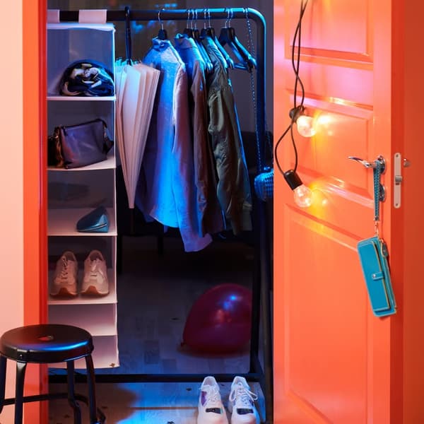Ar zilu gaismu izgaismots drēbju skapis ar drēbēm, apaviem, iekaramo plauktu un atvērtām durvīm oranžā krāsā.