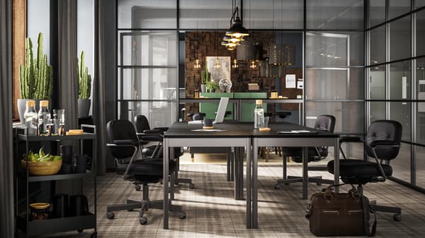 أربع طاولات IDÅSEN لون أسود/رمادي داكن مع كراسي سوداء معروضة في غرفة اجتماعات ذات جدران زجاجية.