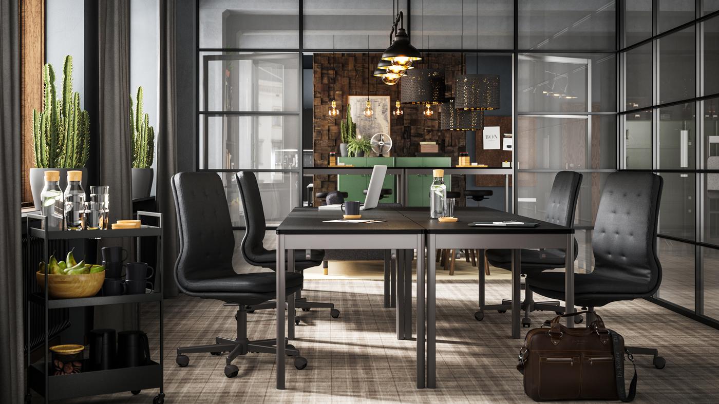 أربعة طاولات IDÅSEN سوداء/رمادي داكن مع كراسي رمادية داكنة معروضة في غرفة اجتماعات بجدران زجاجية.