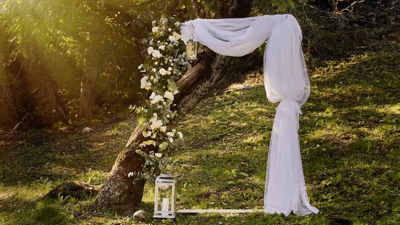 Arco de boda en un jardín con telas y flores; imagen que conduce a ideas de productos para bodas y mesas de regalos.