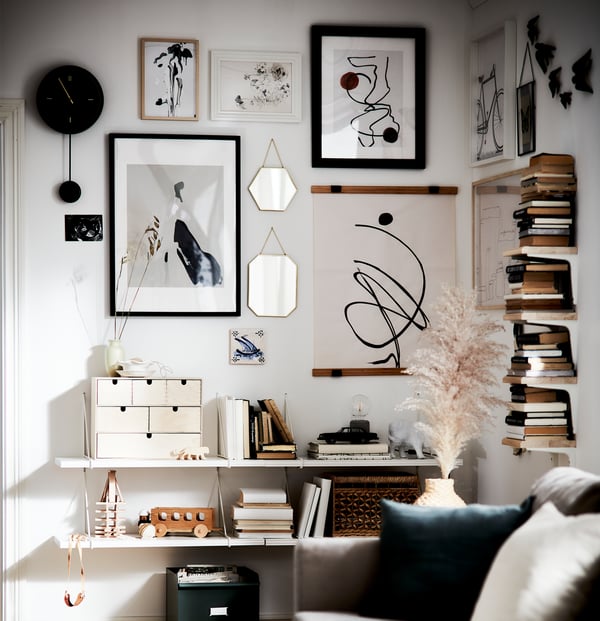 Área de uma sala de estar com livros em segunda mão, destaques em materiais naturais e uma galeria de arte em branco, preto e bege.