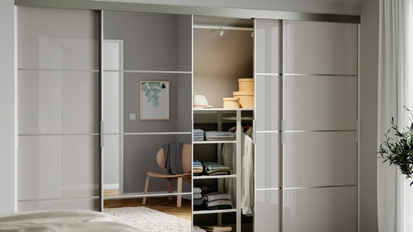 Armari amb portes corredisses SKYTTA en acabat brillant, una d’elles oberta mostrant prestatgeries i roba ordenada a l’interior.