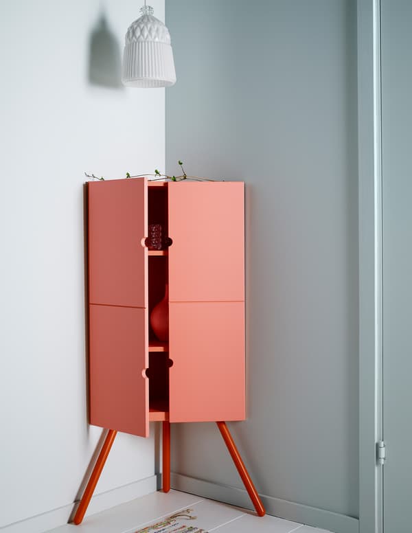 Armari cantoner d’IKEA de fusta de color rosa amb una pantalla de llum de vidre blanca penjada a dalt.