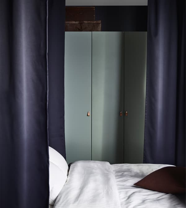 Armari PAX amb portes amb frontisses de color gris-verd en un dormitori amb cortines fosques al voltant del llit.