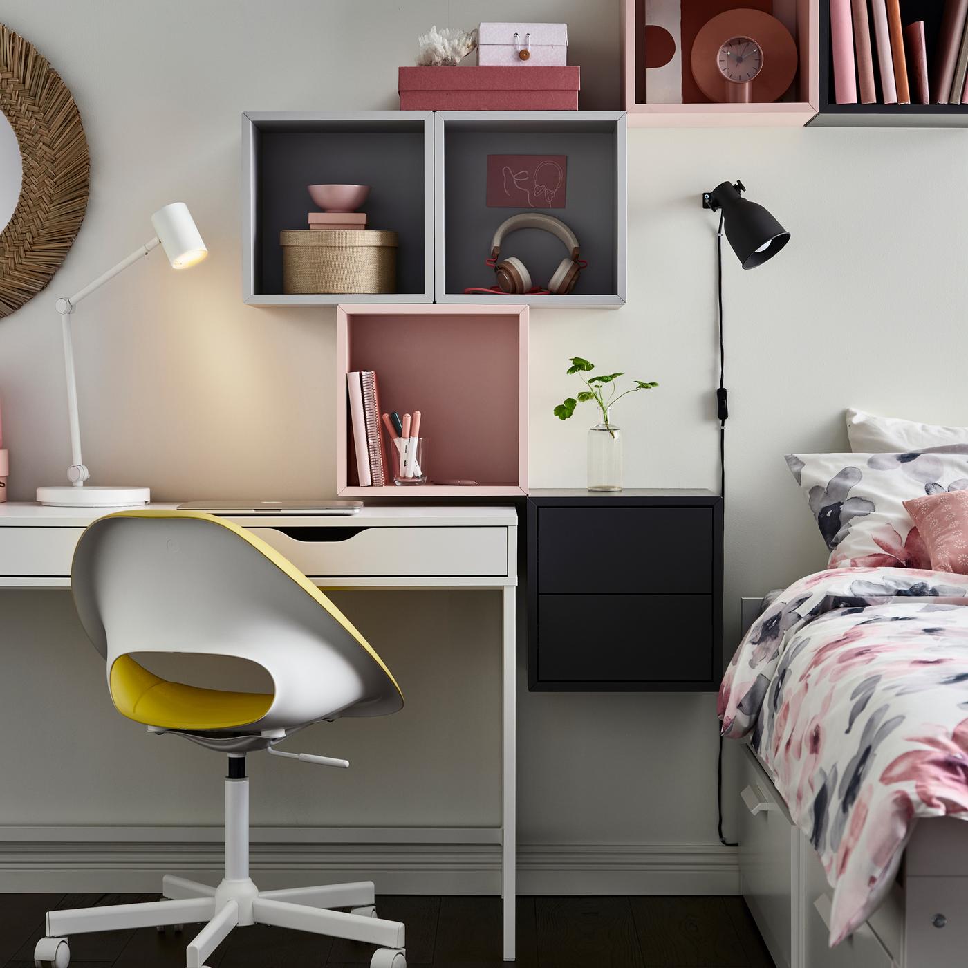 Armarios EKET de cor gris e rosa enriba dun escritorio ALEX branco e un diván BRIMNES branco con roupa de cama LAPPNYCKLAR en varias cores.