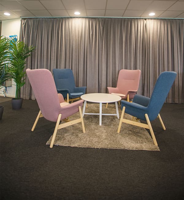 Armchairs are placed facing each other with a white side table with a grey curtain in the background.