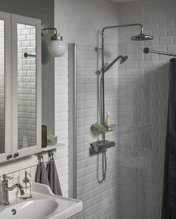 Armoire à miroir et lavabo en blanc, devant une douche carrelée de blanc avec une tête de douche et une étagère chromées.