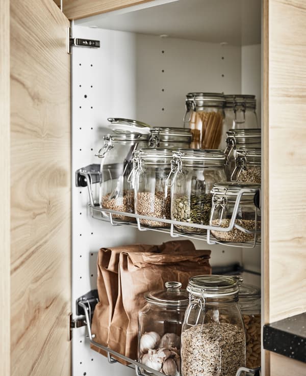 Armoire haute avec porte en frêne ouverte, dévoilant des tiroirs en fil garnis de bocaux en verre transparents.