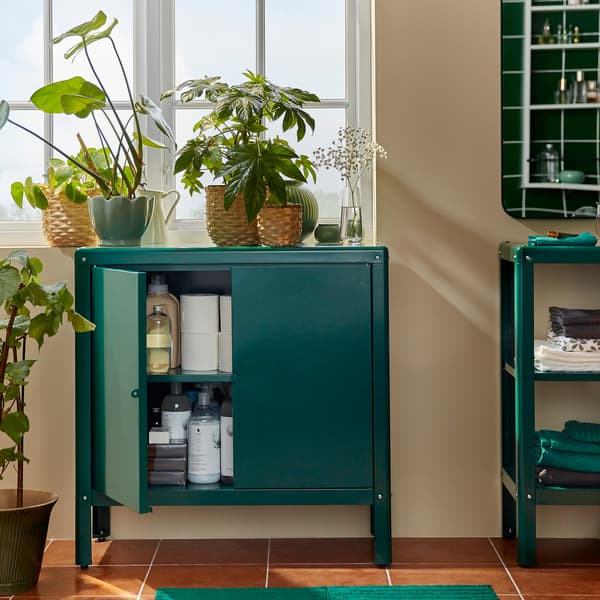 Armoire KOLBJÖRN verte devant une fenêtre. Par la porte ouverte, on peut voir du papier hygiénique et des détergents rangés à l’intérieur.