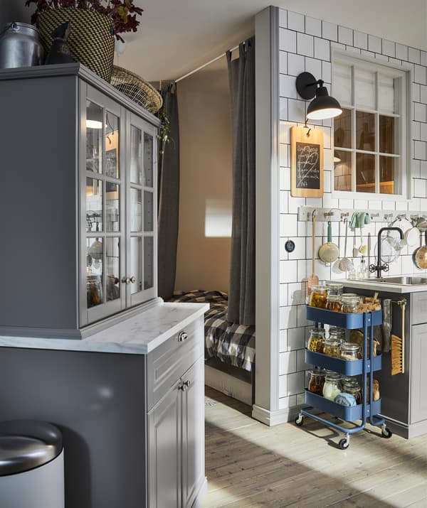 Armoires de cuisine grises, une desserte bleue et des crochets fixés le long d’un mur de carrelages blancs au-dessus d’un évier. 