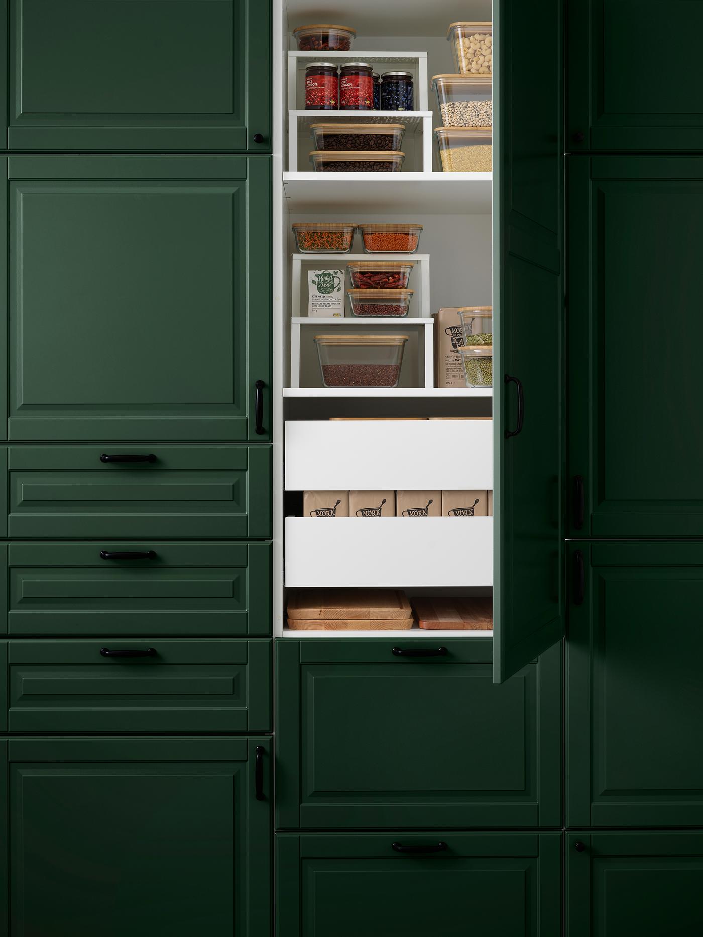 Armoires de cuisine vert foncé avec une porte ouverte, où des aliments secs sont rangés sur des étagères et tablettes blanches.